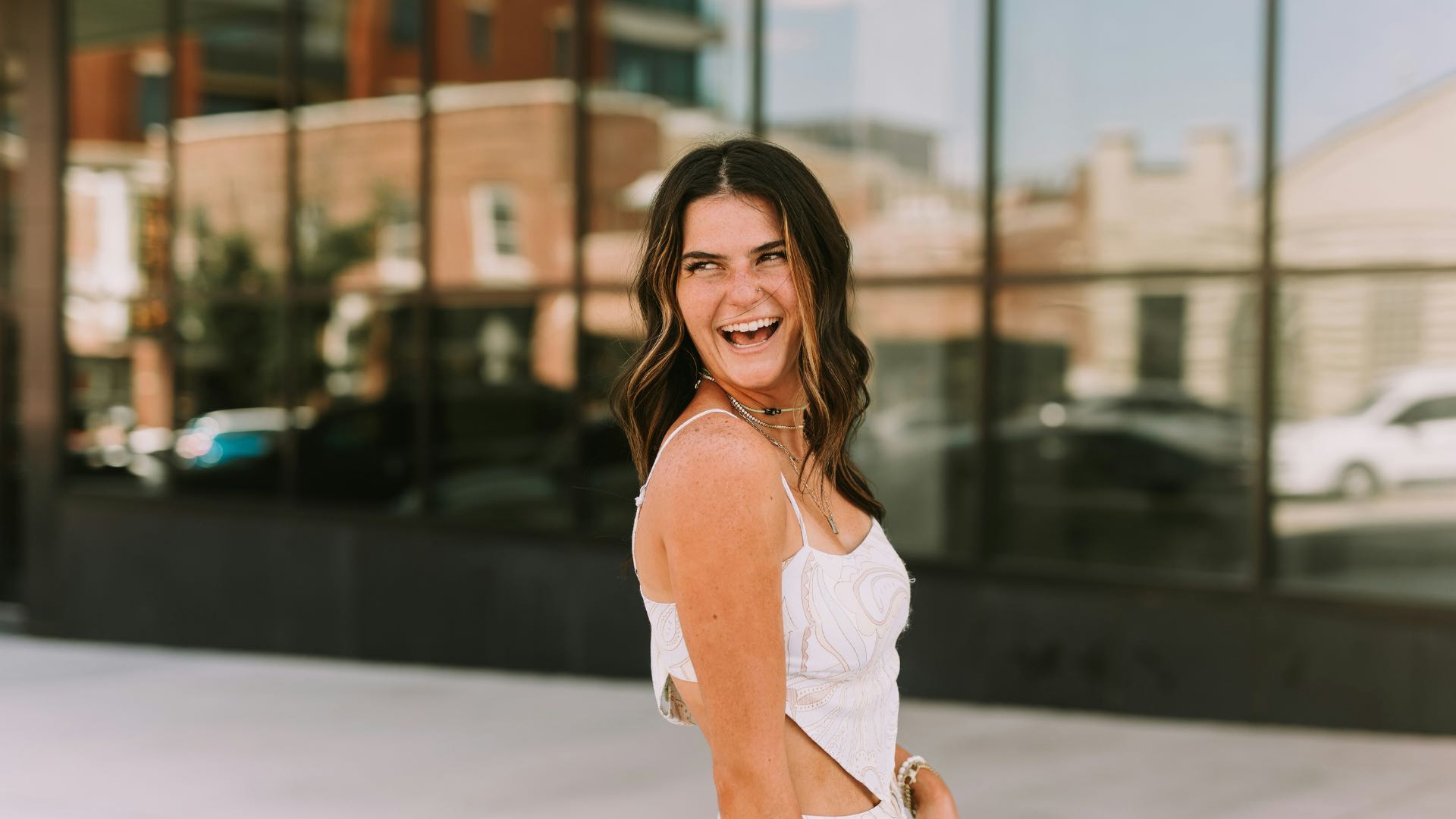 Woman In White Top Looking Behind Shoulder And Laughing