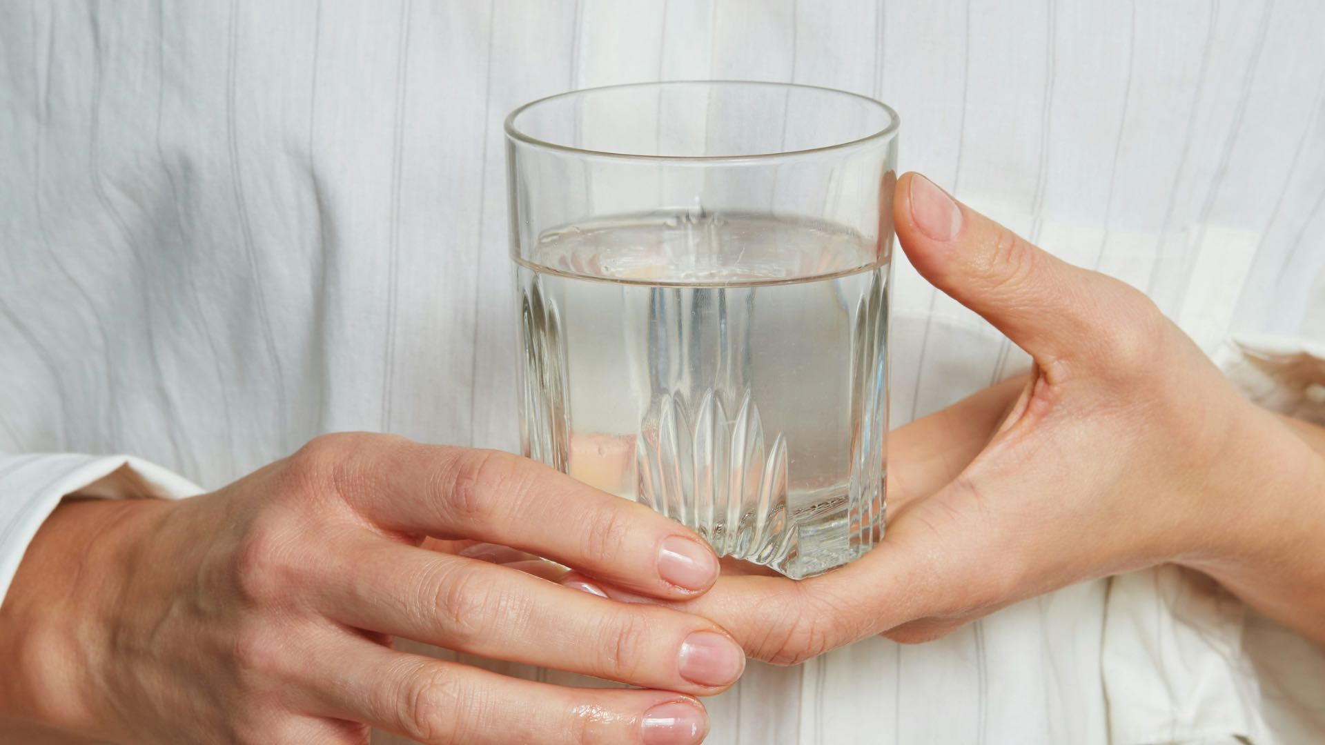 Person Holding Glass Of Water In Front Of Chest