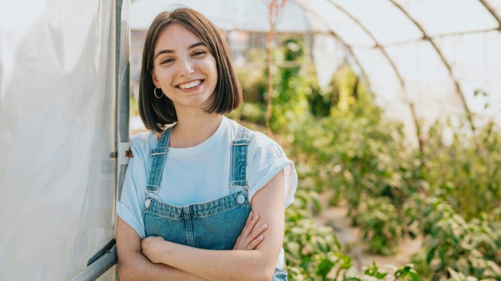 Woman In Overalls In A Greenhouse Smiling