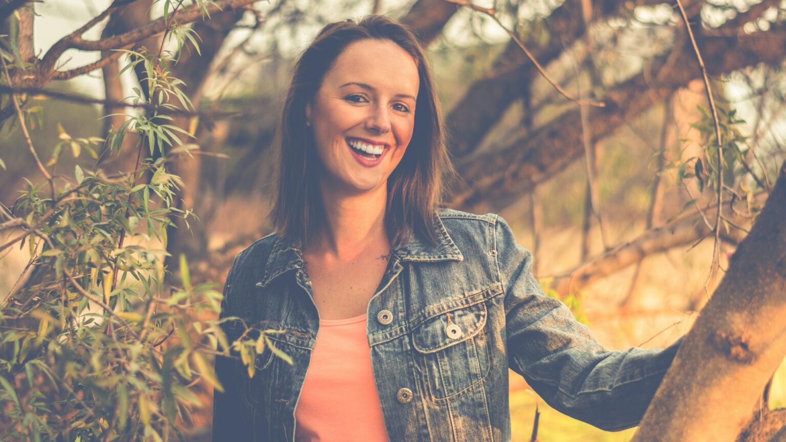 Woman In Denim Jacket Smiling With Trees In The Background