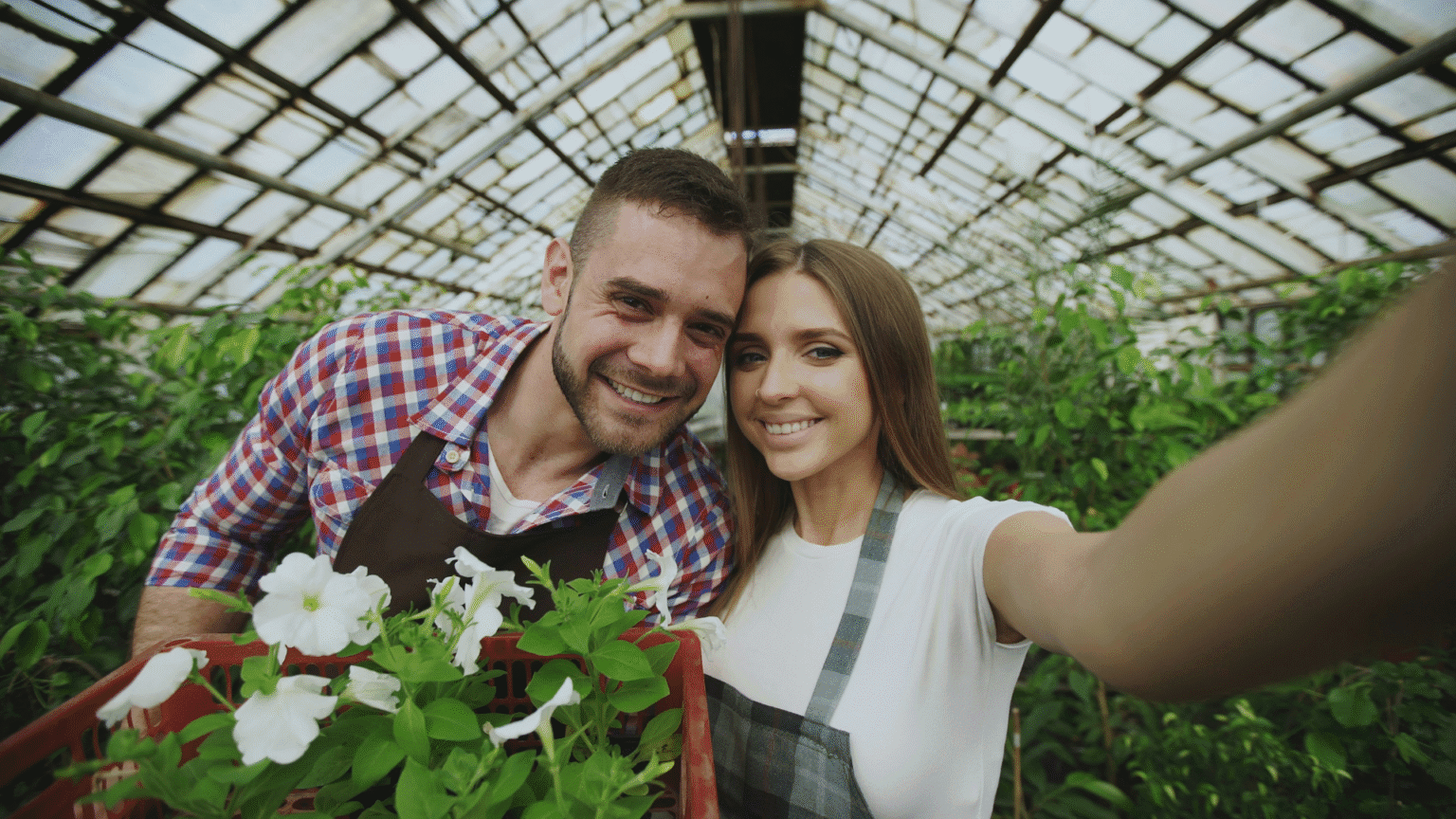 Man And Woman Smiling In Greenhouse With Flowers