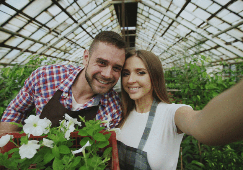 Man And Woman Smiling In Greenhouse With Flowers