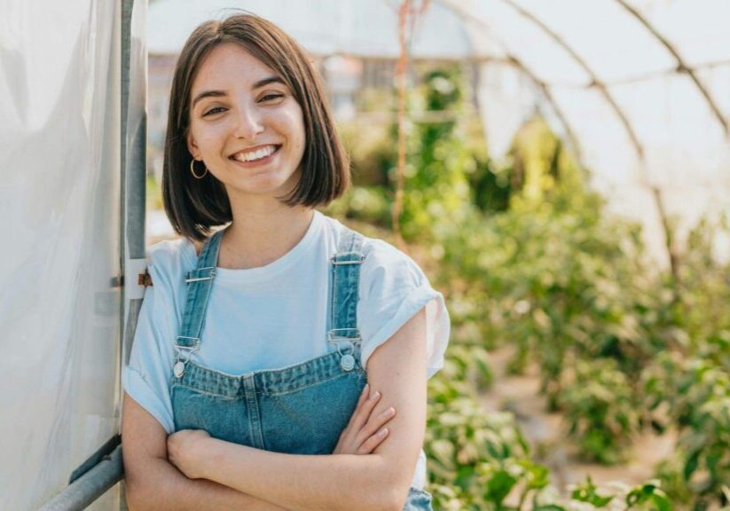 Woman In Overalls In A Greenhouse Smiling